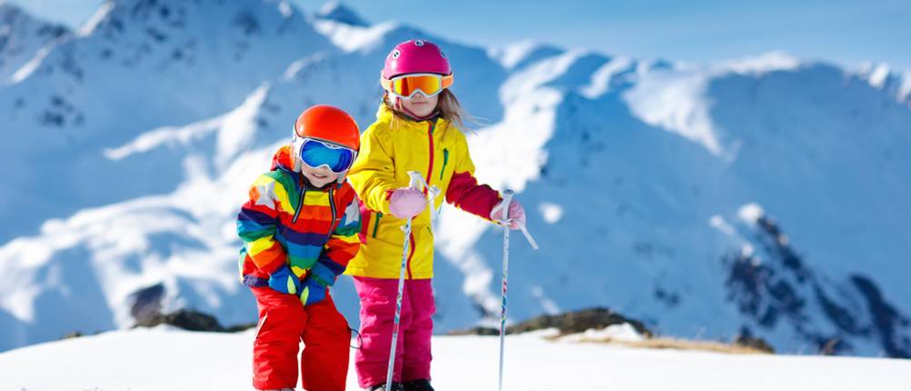 zwei Kinder mit Skihelmen auf ihren Skiern im Schnee