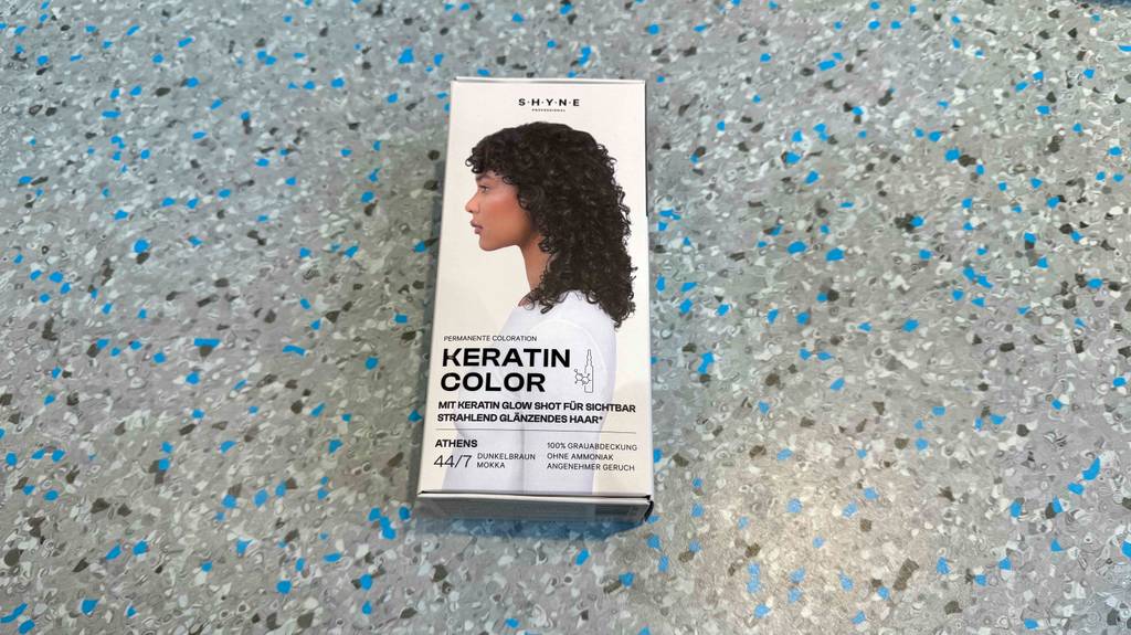 Die Verpackung von getesteter Haarfarbe dunkelbraun liegt auf einem gesprenkelten Boden.