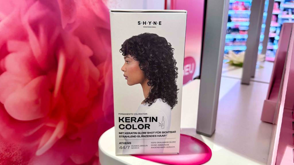 Eine Packung Haarfarbe dunkelbraun steht zum testen auf einem weißen Regal mit rosa Hintergrund.