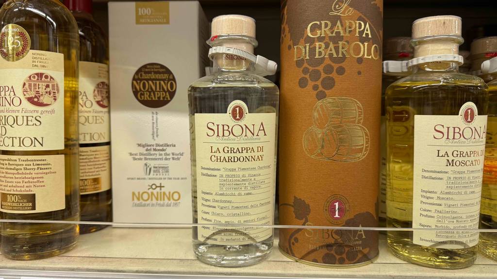 Ein gtetesteter Chardonnay Grappa in der Flasche mit Holzkorken steht neben weiteren Spirituosen auf einem Ausstellungsregal.
