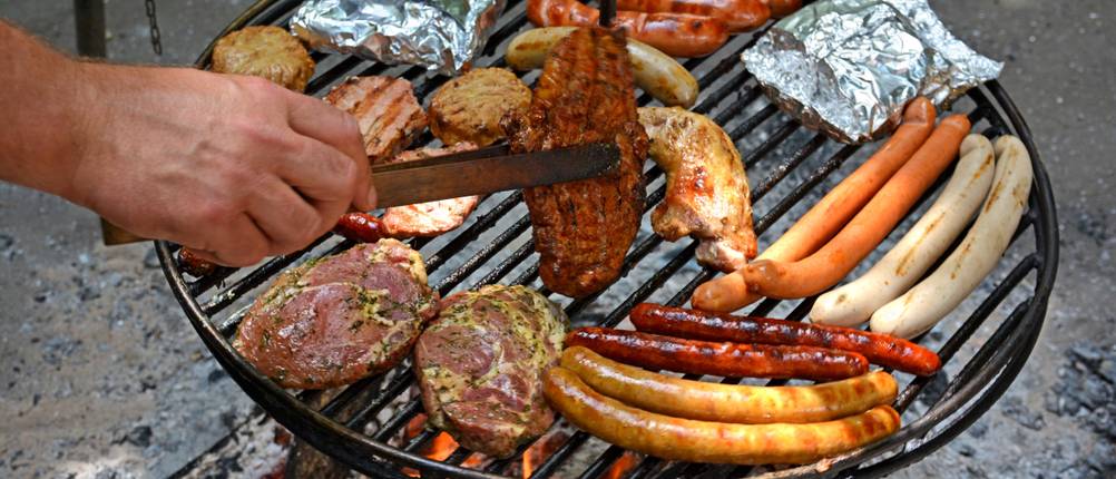 Schwenkgrill mit diversem Grillgut über einer offenen Flamme.