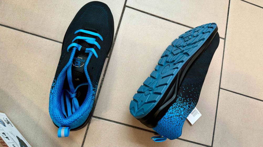 Getestet: Ein Paar Sicherheitsschuhe-S1 Herren auf einem Fließenboden, einer steht, einer liegt auf der Seite.