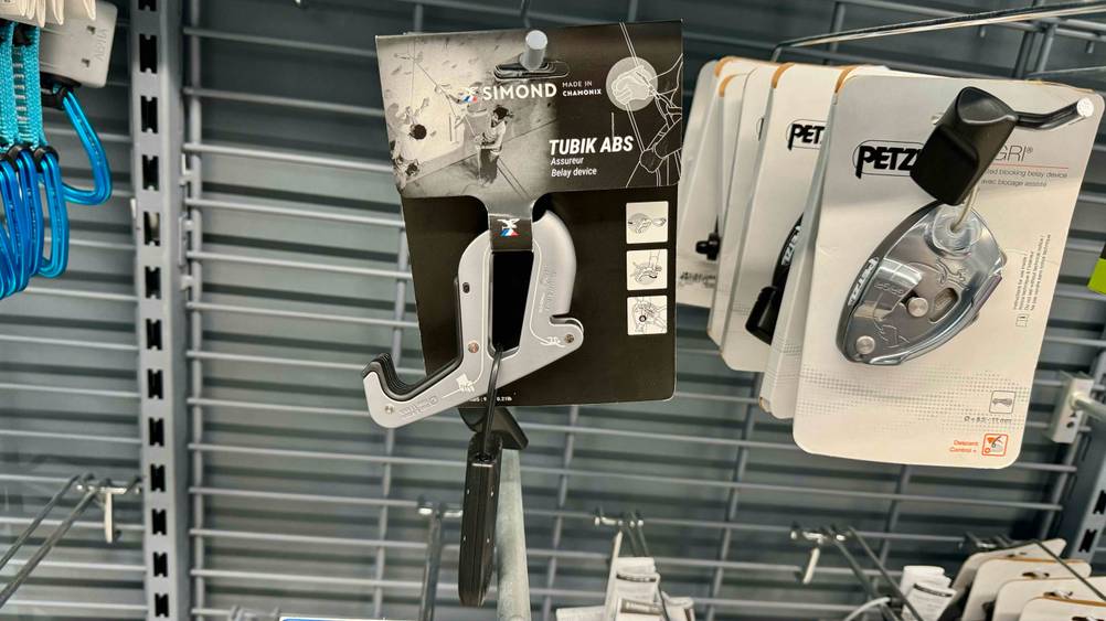 In einem Regal hängt neben anderen Produkten ein Sicherungsgerät für das Klettern im Test.