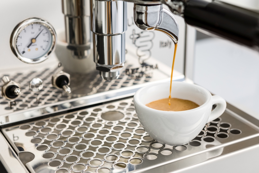 Espresso läuft aus einer Siebträgermaschine in eine weiße Tasse.