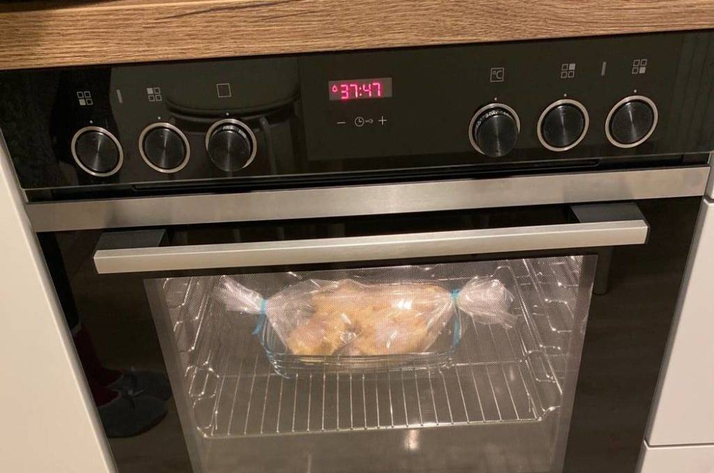 Einbauherd-Set-Test: Vorderansicht eines Modells von Siemens mit beleuchtetem Backofen inklusive Braten in weißer Küchenzeile auf hellem Holzboden.
