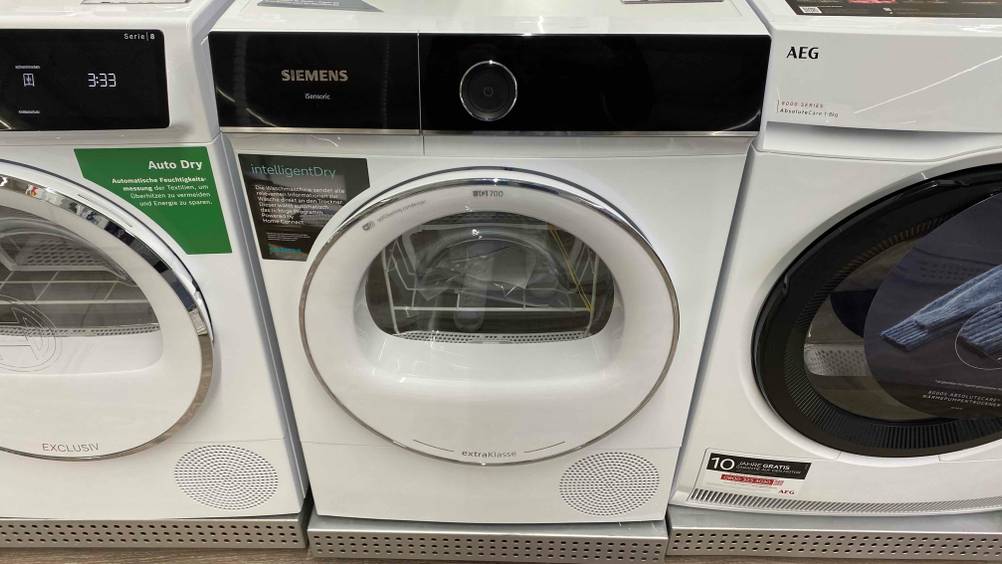Im Test: Ein Siemens-Trockner von vorne zwischen anderen Geräten auf einem Metallsockel.
