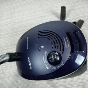 Oberseite des Siemens VS06B1110 Staubsaugers mit Bedienelementen, Lüftungsschlitzen und Logo. Der Saugschlauch ist vorne angeschlossen.