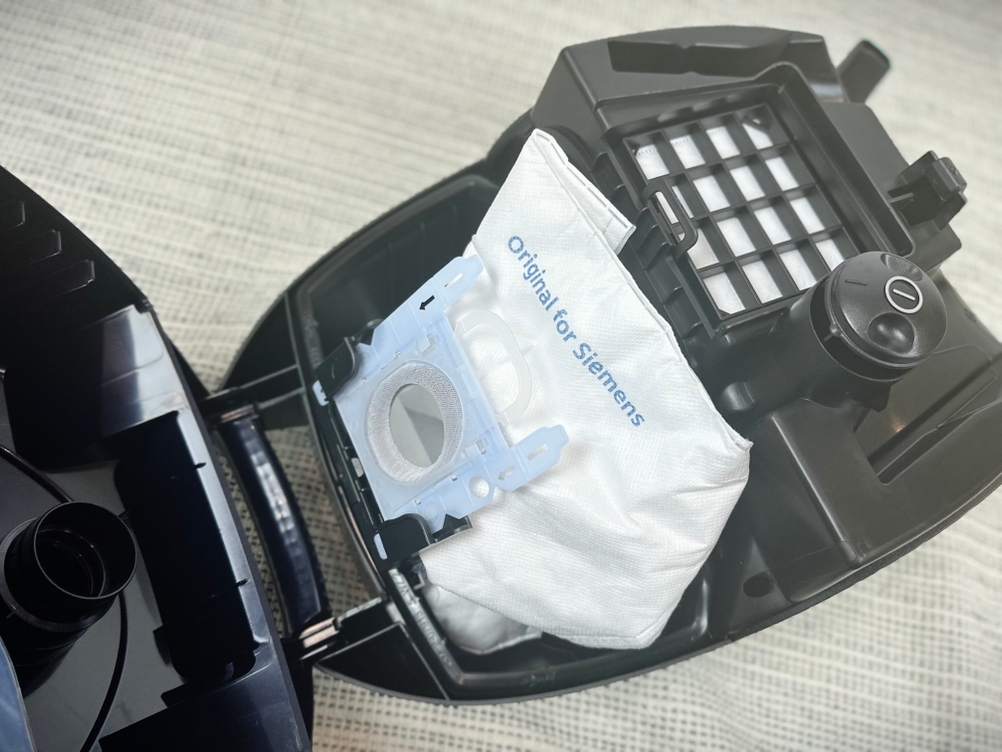 Der Staubbeutelraum des Siemens VS06B1110 ist geöffnet. Ein Beutel mit der Aufschrift „Original for Siemens“ ist eingesetzt, daneben der HEPA-Filter.
