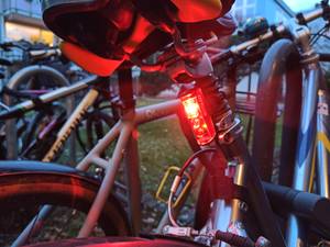 Ein Fahrrad an einem gut gefüllten Fahrradständer mit einem rot leuchtenden Rücklicht