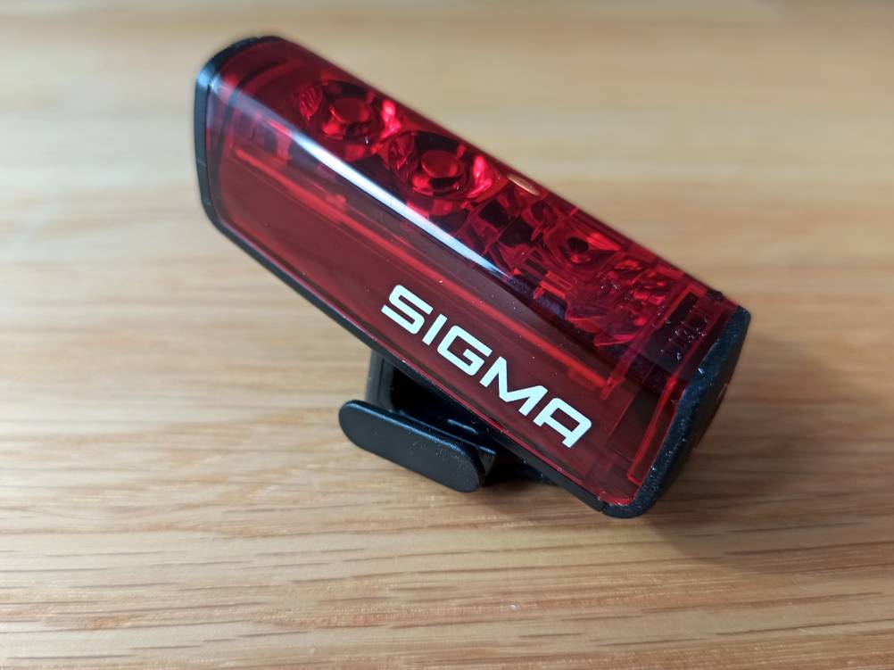 Ein rotes Fahrrad-Rücklicht der Firma Sigma auf einem Holztisch