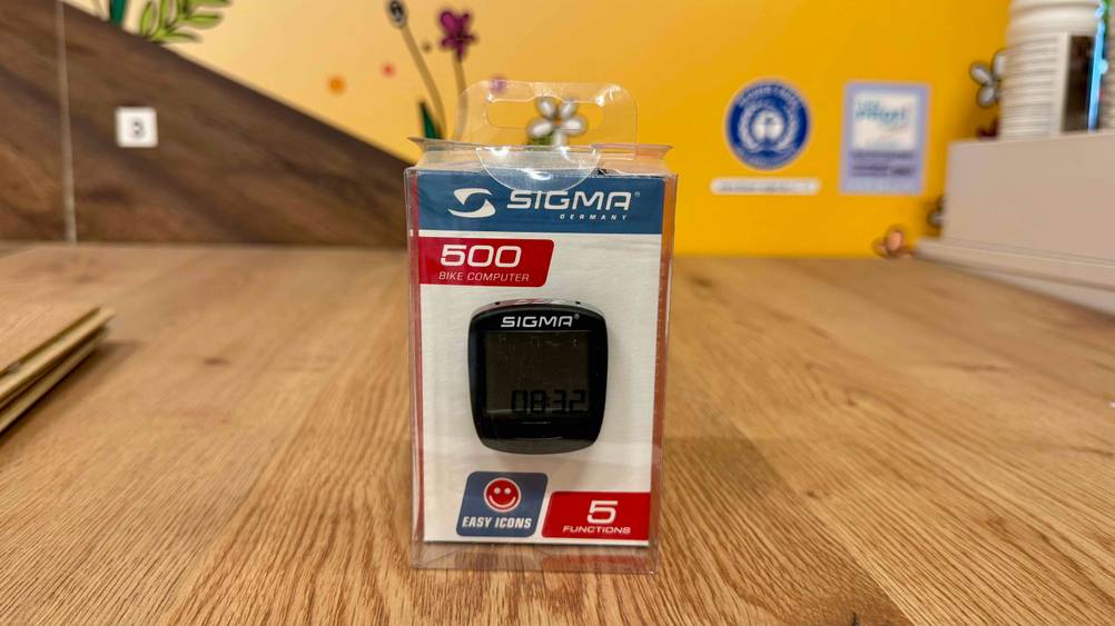 Auf einer Holzfläche steht der verpackte Sigma-Fahrradcomputer im Test.