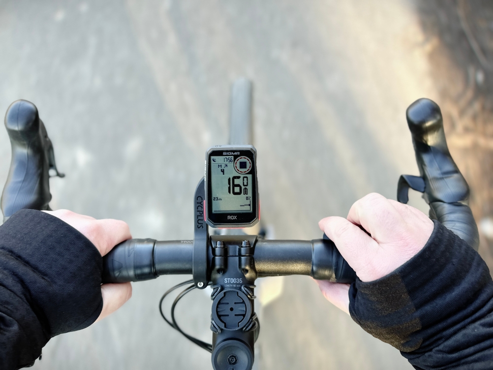 Das Sigma Sport ROX 4.0 zeigt während der Fahrt Geschwindigkeit und Distanz an. Zwei Hände halten den Lenker bei der Nutzung.