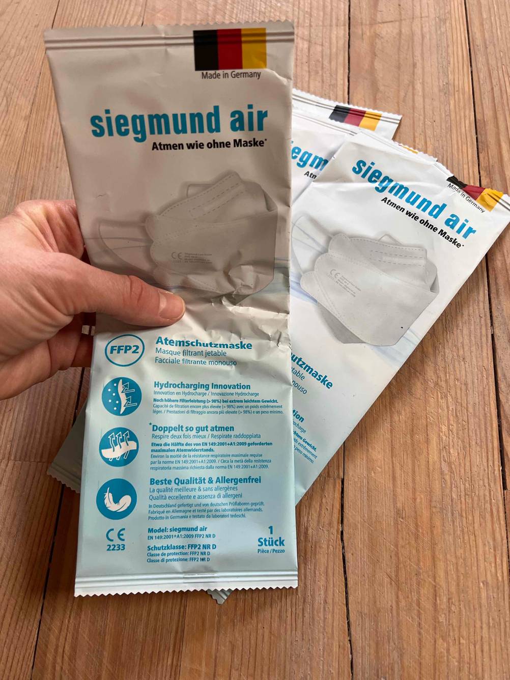 Eine Hand hält eine Packung der getesteten FFP2-Masken nach oben vor zwei weitere Packungen.
