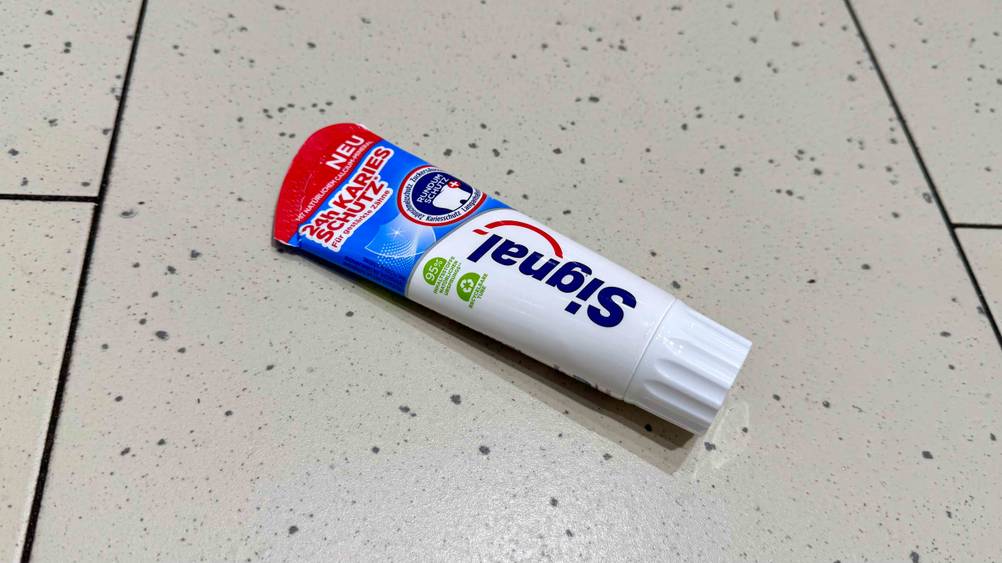 Auf einem hellen Boden liegt horizontal eine Tube der Signal-Zahnpasta im Test.