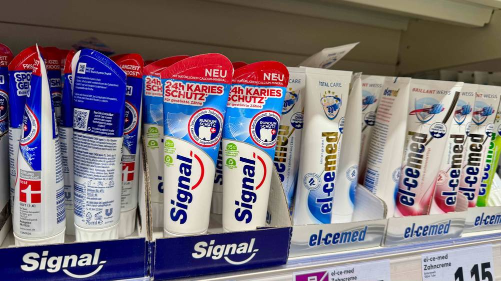 Mehrere Tuben der getesteten Signal-Zahnpasta in einem Verkaufsregal neben anderen Produkten.