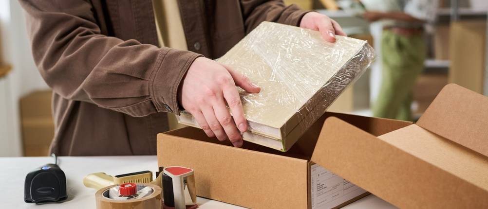 Person verpackt einen Gegenstand sorgfältig in einem Versandkarton.