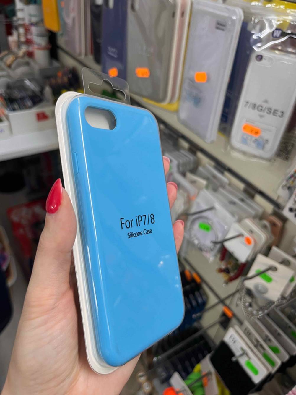 iPhone-8-Hüllen im Test: Eine Hand hält eine hellblaue Hülle in der Originalverpackung vor einem Verkaufsregal.