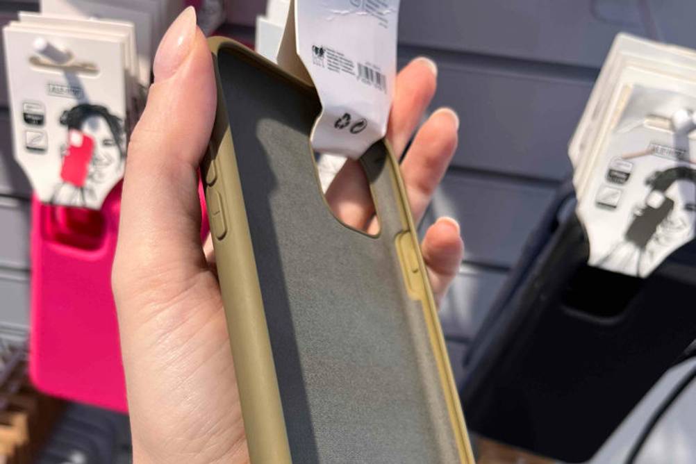 Hand hält getestete iPhone 11 Pro Max Hülle in Olivgrün vor einem Verkaufsstand.