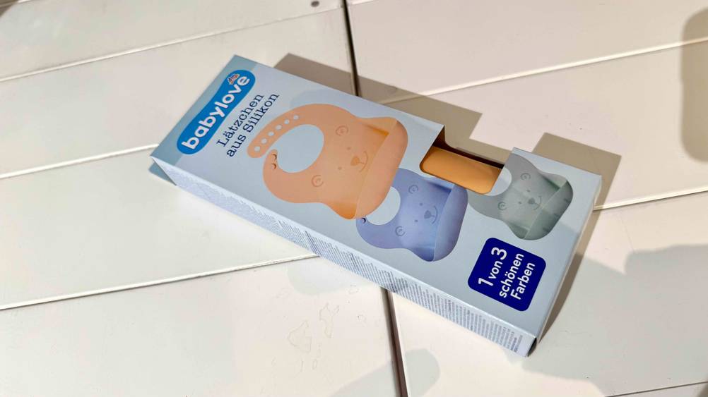 Ein verpacktes Silikon-Lätzchen im Test liegt auf einer hellen Fläche.