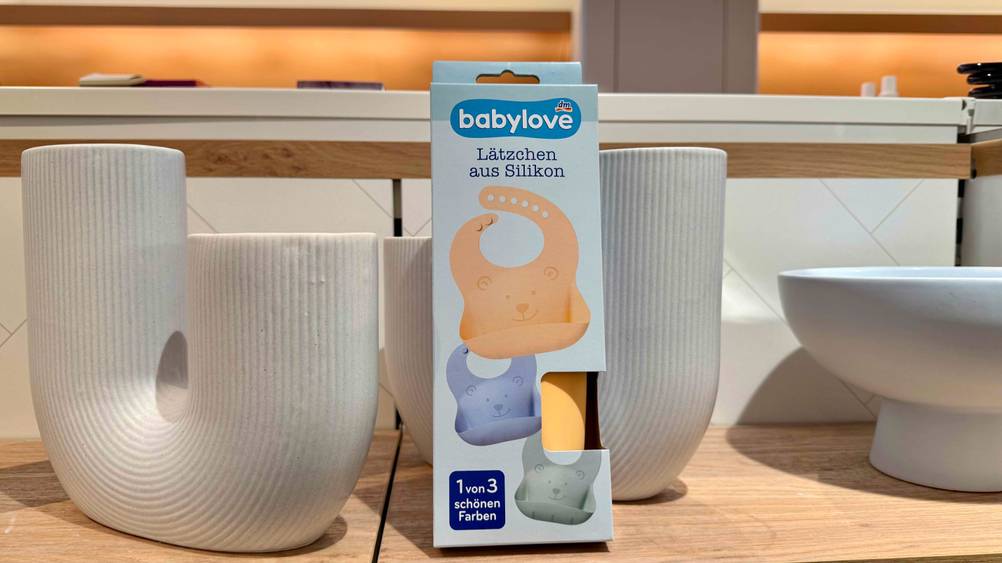 Ein getestetes Silikon-Lätzchen lehnt in seiner Verpackung an einer Vase.
