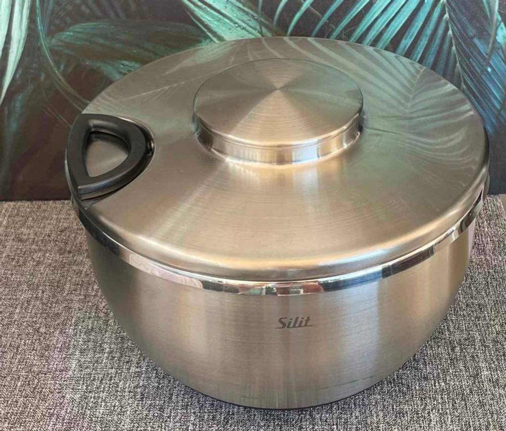 Seitliche Ansicht einer getesteten Edelstahl-Salatschleuder von Silit, die vor einem Palmenbild steht.