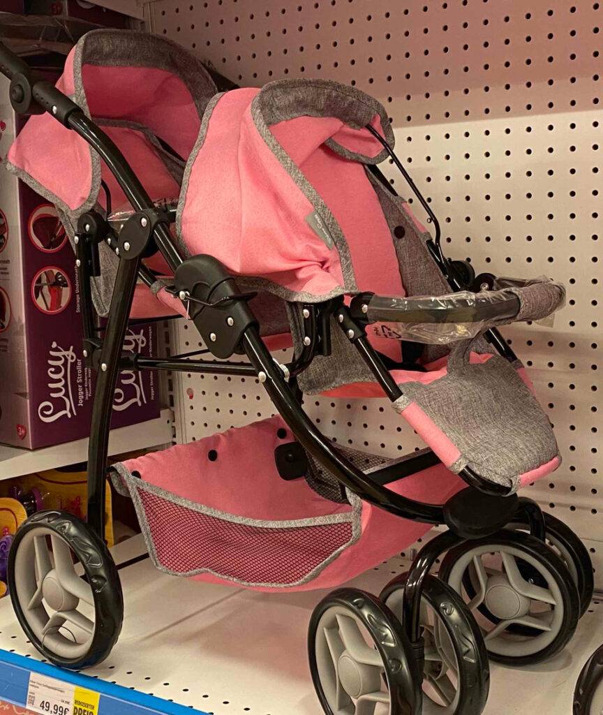 Im Test: Ein Zwillingspuppenwagen in Rosa-Grau steht auf einer Ausstellungsfläche in einem Spielwarengeschäft.