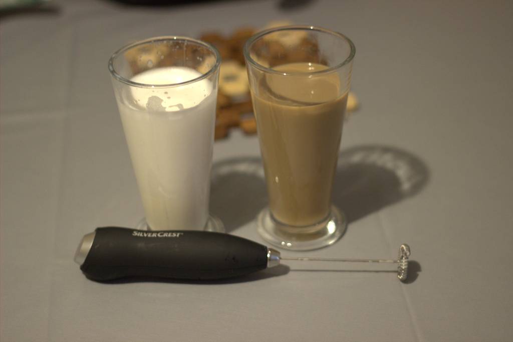 Ein getesteter Hand-Milchaufschäumer liegt vor zwei Gläsern mit Milch undKaffee.