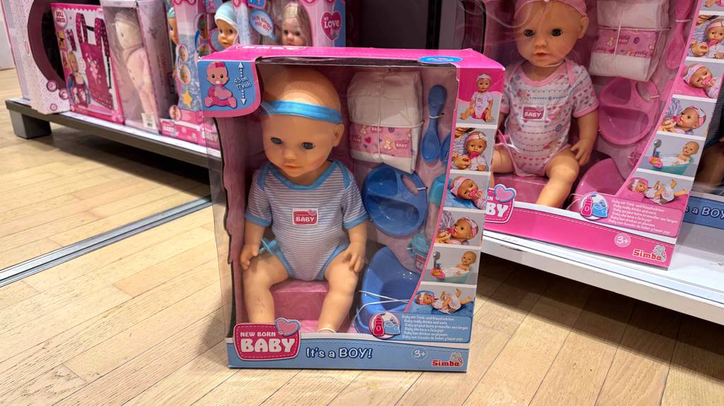 Babyborn getestet: Die verpackte Ausführung Boy steht vor einem Regal mit weiteren Puppen.