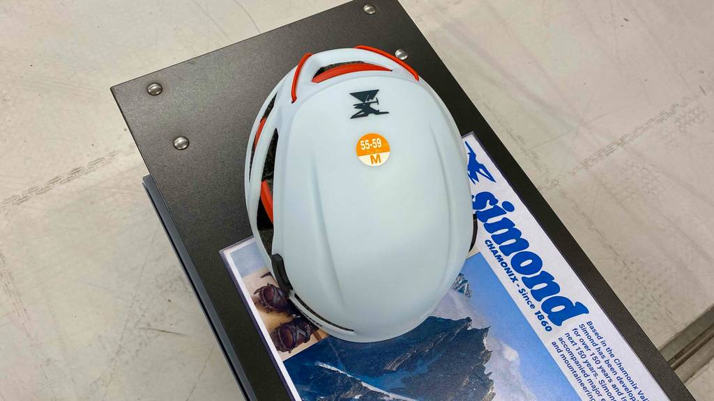 Kletterhelm im Test: Ein weißer Helm in Größe M liegt auf einer Werbefläche der Marke Simond, von oben betrachtet.