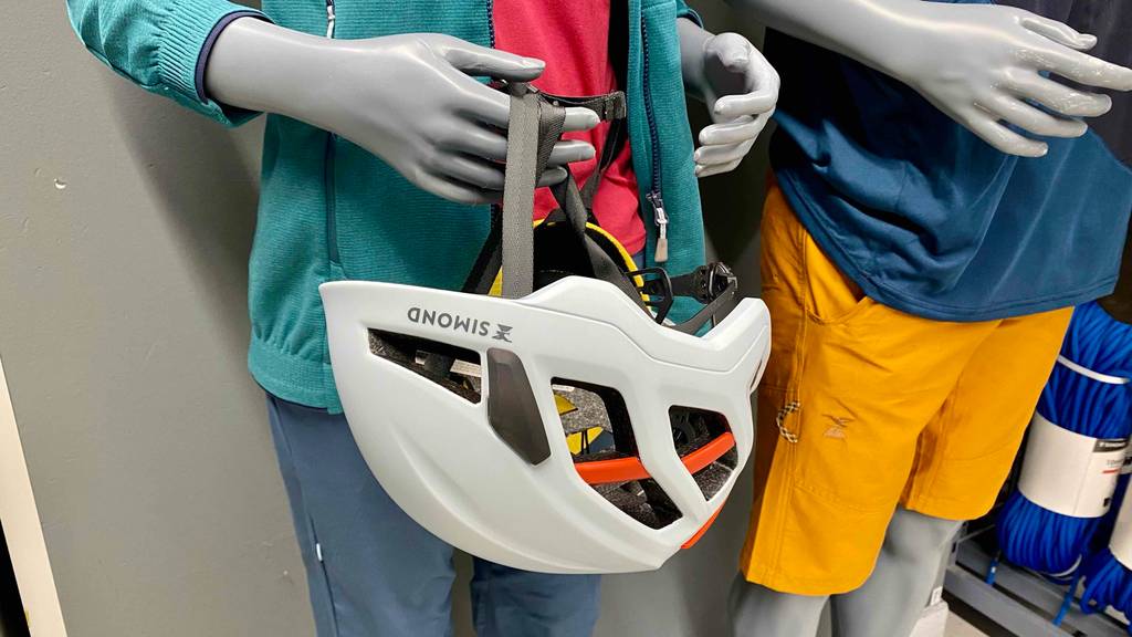 Ein getesteter Kletterhelm von Simond hängt mit dem Riemen an der Hand einer Schaufensterpuppe.
