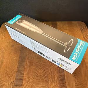 Der Karton des Simpletaste-Milchaufschäumer liegt auf einer Holzplatte