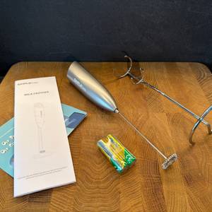 Der Lieferumfang des Simpletaste-Milchaufschäumer liegt auf einer Holzplatte