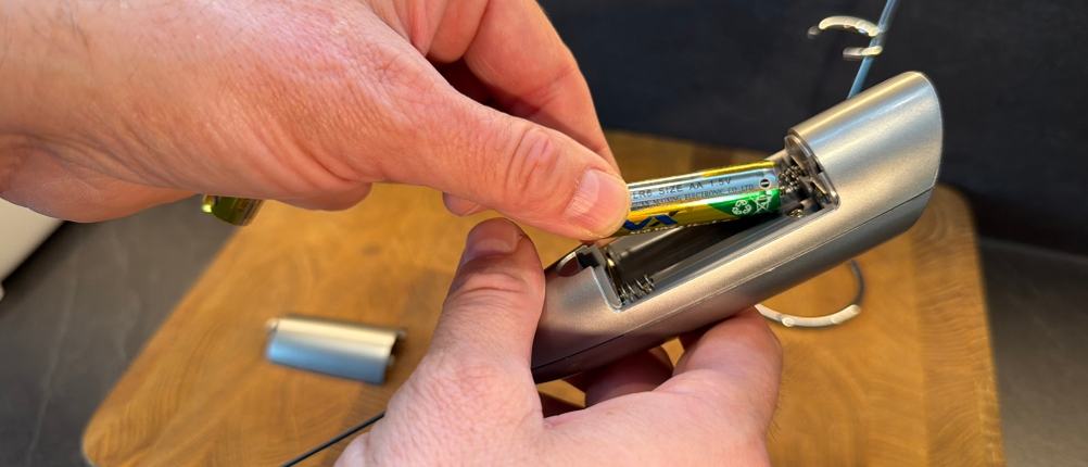 Eine Hand legt eine Batterie in den Simpletaste-Milchaufschäumer