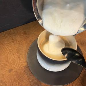 Milchschaum vom Simpletaste-Milchaufschäumer wird in eine Tasse mit Kaffee geschüttet