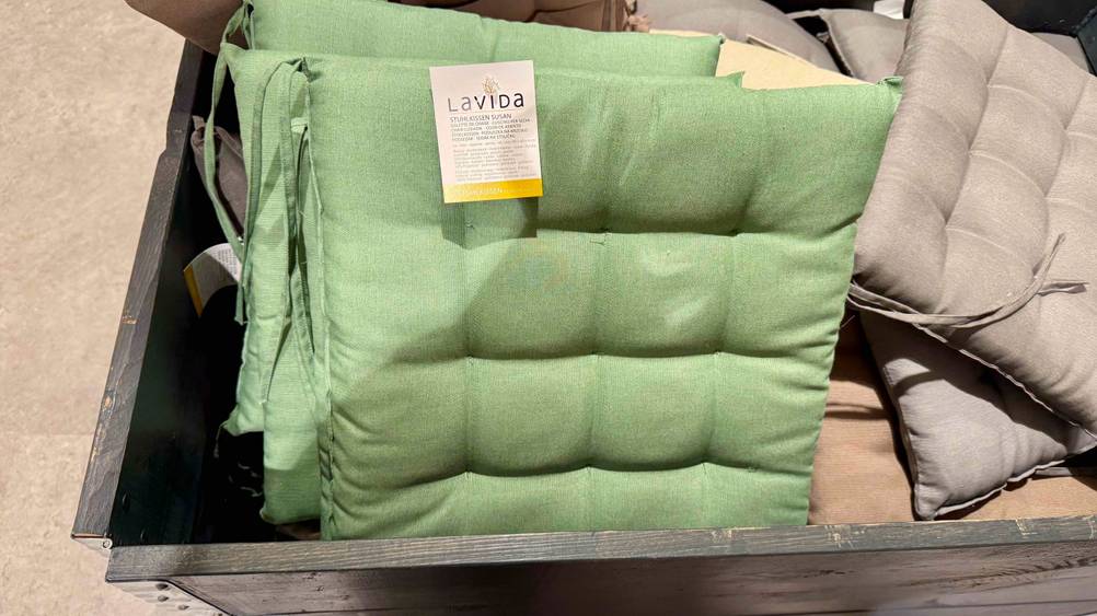 Ein getestetes Sitzkissen mit Label in einer Holzbox mit anderen Kissen.