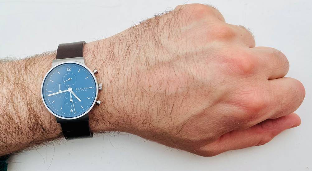 Eine Skagen-Uhr im Test an einem Männerhandgelenk auf einer hellen Fläche liegend.