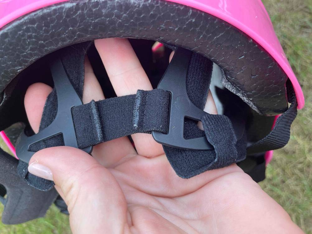 Nahaufnahme der Verstellbänder hinten an einem getesteten Skaterhelm für Kinder von einer Hand gehalten.