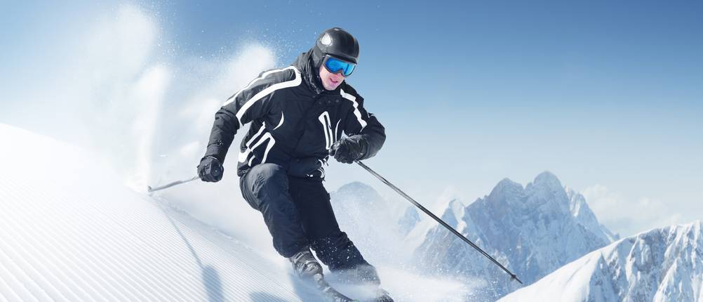 Skianzüge für Herren im Test: Skifahrer in schwarzem Skianzug fährt durch Schnee.