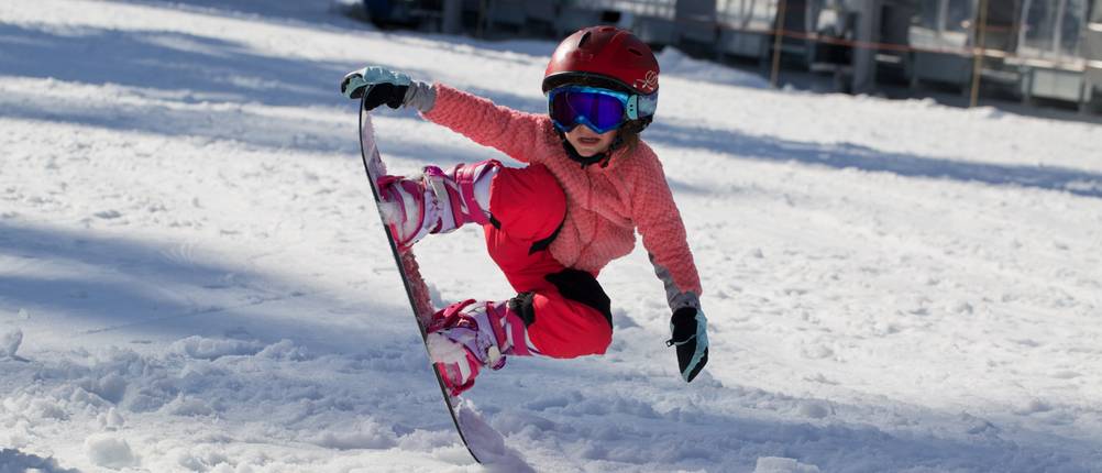 Skibrillen für Kinder im Test: Ein Mädchen mit Snowboard, Helm und Skibrille. 