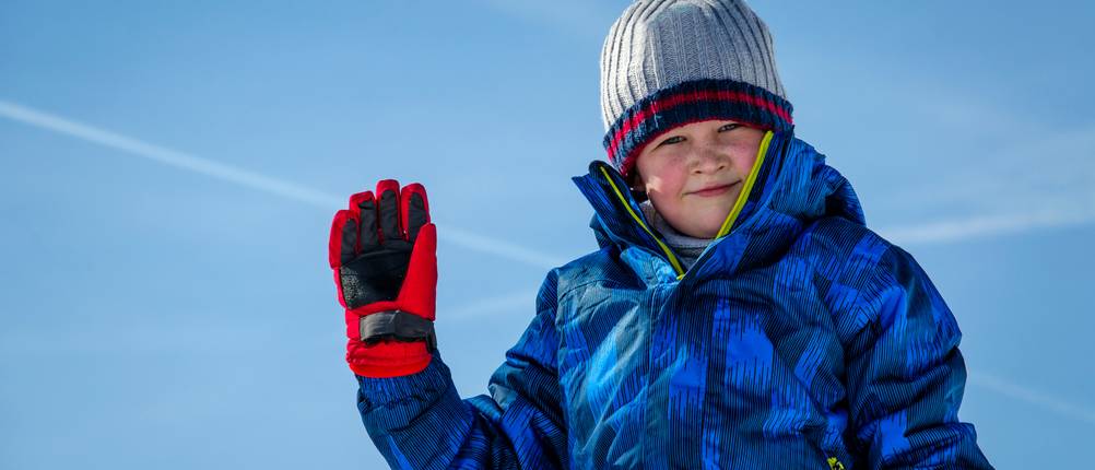 Skijacke Kinder Jungen Test: Junge winkt in Skijacke vor blauem Himmel