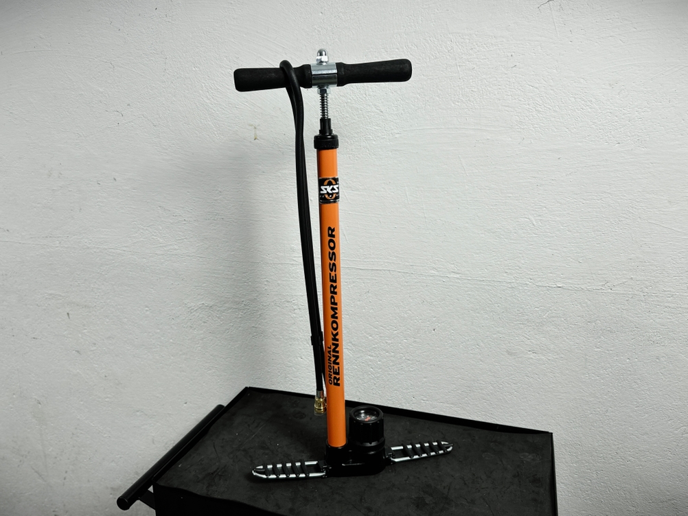 Die SKS Rennkompressor 2192525400 steht senkrecht auf einer schwarzen Werkbank. Die orangefarbene Pumpe ist vollständig montiert.
