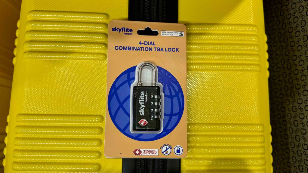 Kofferschloss getestet: Ein Zahlenschloss von Skyflite liegt innerhalb der Originalverpackung auf einem gelben Koffer.