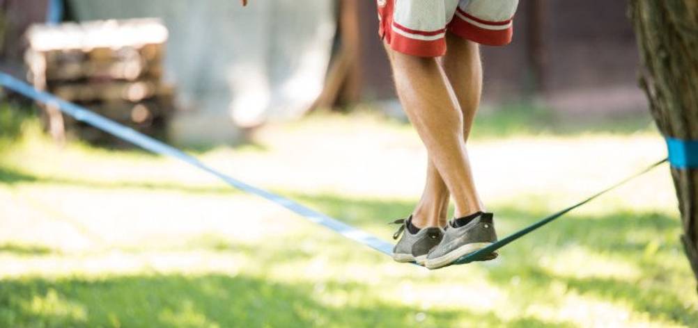 Slackline-Gestelle im Test: Ein Mann in Shorts trainiert im Park auf einer Slackline. Man sieht nur die Beine.