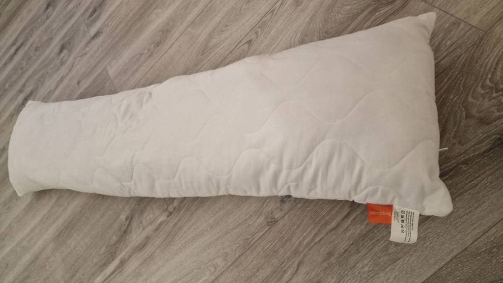 Stäbchenförmiges Sleeping Seitenschläferkissen im Test liegt der Länge nach auf einem Holzboden.
