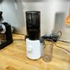 Der Hurom H310A Slow Juicer steht auf einer Holzarbeitsplatte in einer Küche, mit weiteren Geräten im Hintergrund.