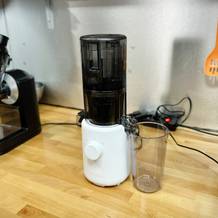 Der Hurom H310A Slow Juicer steht auf einer Holzarbeitsplatte in einer Küche, mit weiteren Geräten im Hintergrund.