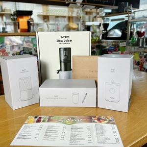 Der Lieferumfang des Hurom H310A Slow Juicers ist auf einem Tisch ausgelegt, daneben die Verpackung und alle enthaltenen Zubehörteile. 