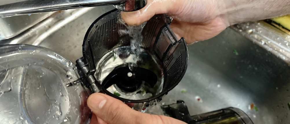 Ein Nutzer reinigt den Hurom H310A Slow Juicer unter fließendem Wasser. Die Einzelteile werden gründlich abgespült.