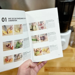 Ein geöffnetes Rezeptbuch für den Hurom H310A Slow Juicer zeigt verschiedene Zubereitungsmöglichkeiten. Es enthält Anleitungen und Bilder zu Obst- und Gemüsesäften.