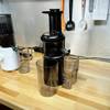 Der Panasonic MJ-L501KXE Slow Juicer steht zusammen mit seinem Zubehör auf einer Arbeitsplatte. Im Hintergrund befindet sich ein weiterer Slow Juicer in Weiß.